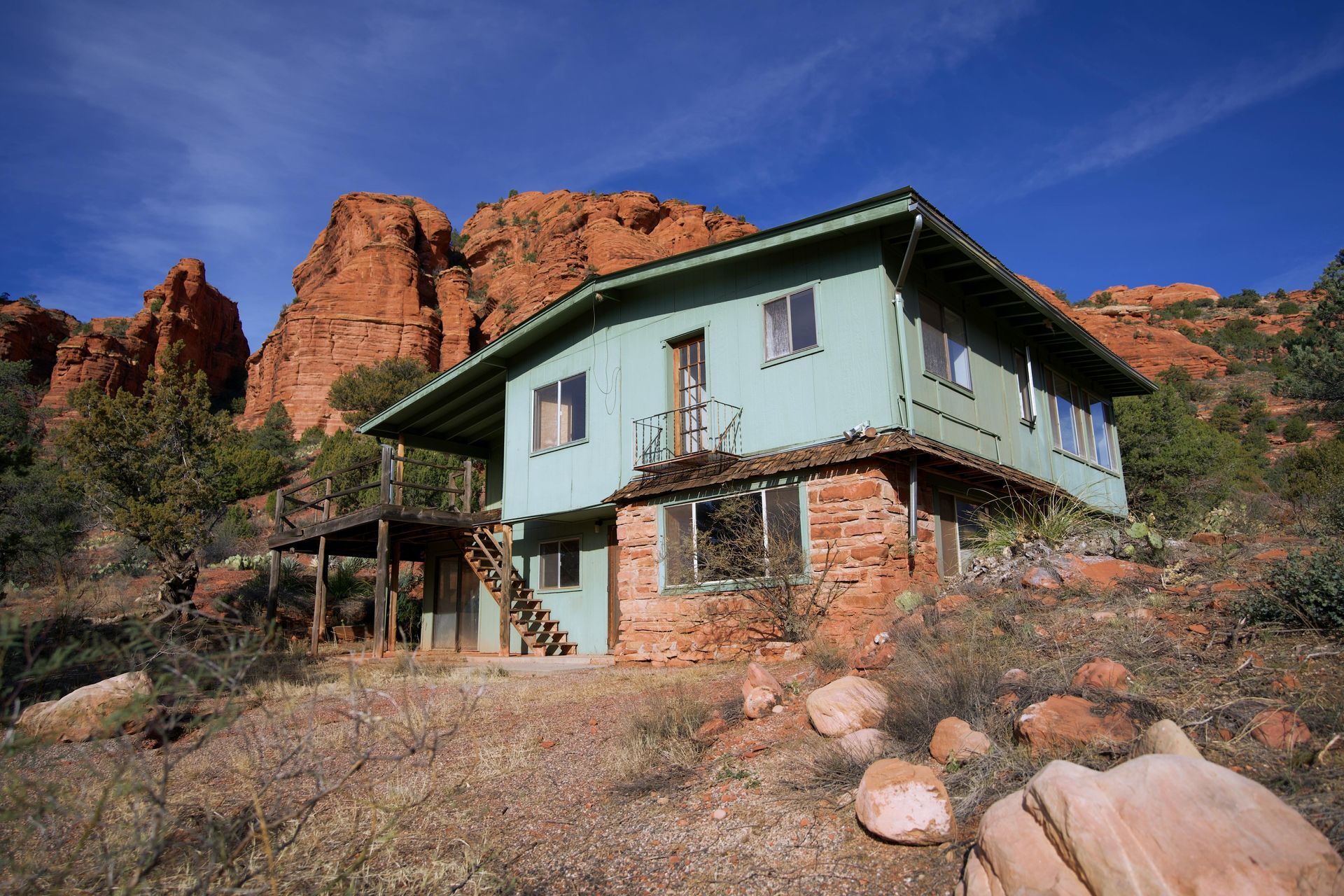 A green house is sitting on top of a hill next to a mountain.