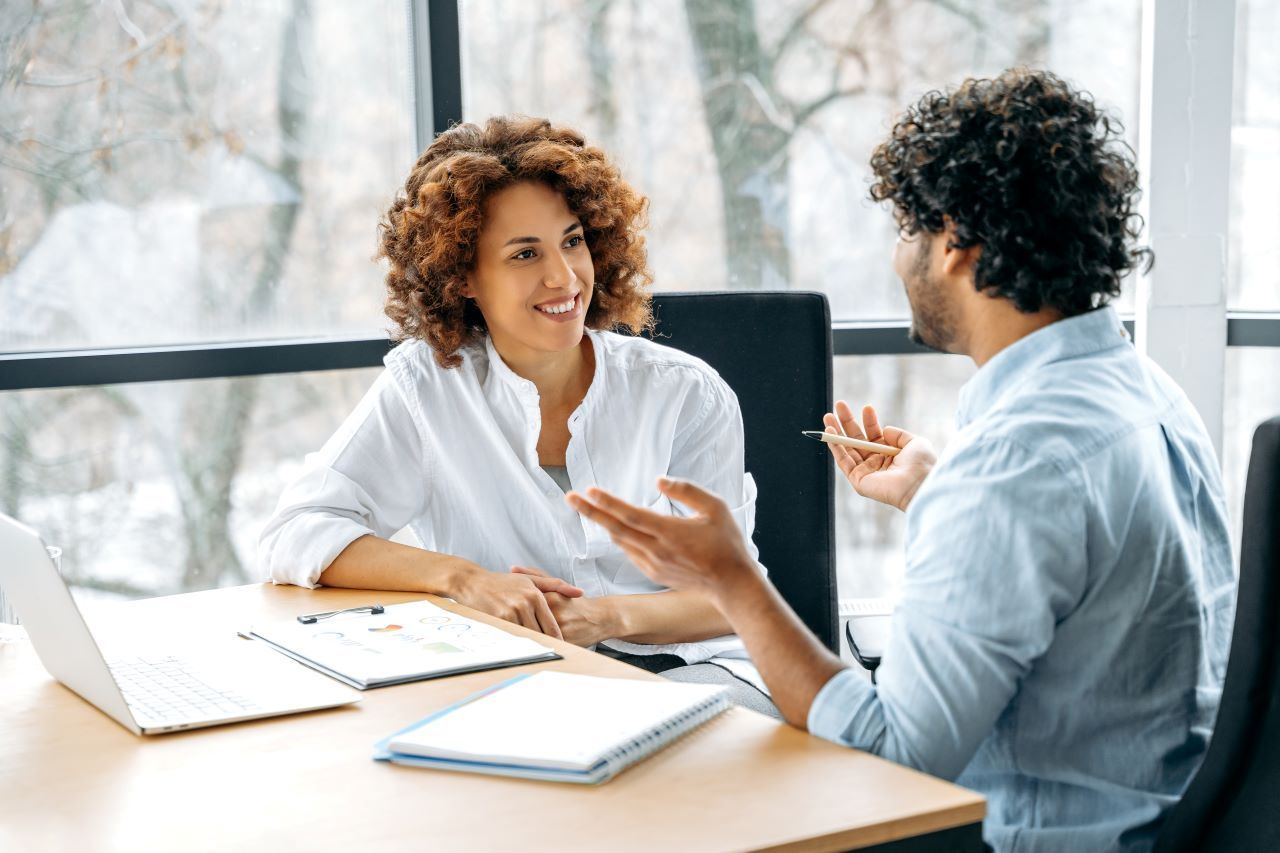 Two men in a meeting, one pointing at a tablet. Coffee cups on a white table.