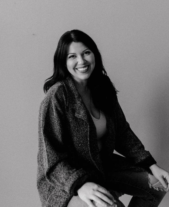A woman is sitting on a stool and smiling in a black and white photo.