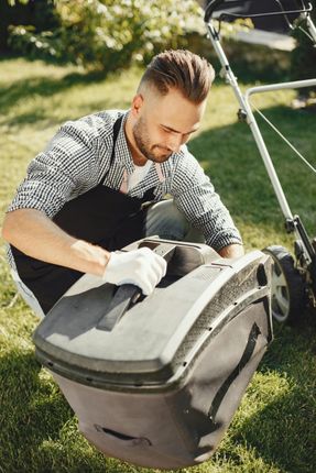 A man is repairing a lawn mower on the grass.