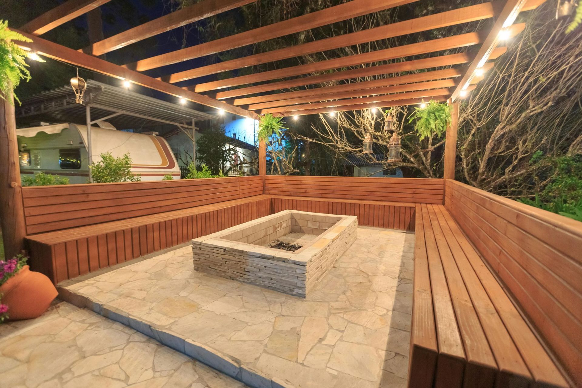 A large stone fire pit under a wooden pergola with ample seating