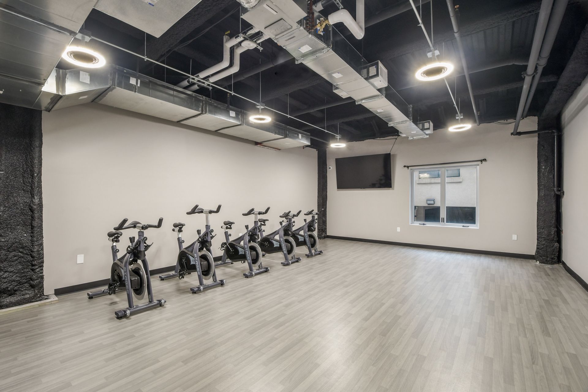 Spin class studio with exercise bikes, TV, and window; gray and black decor.