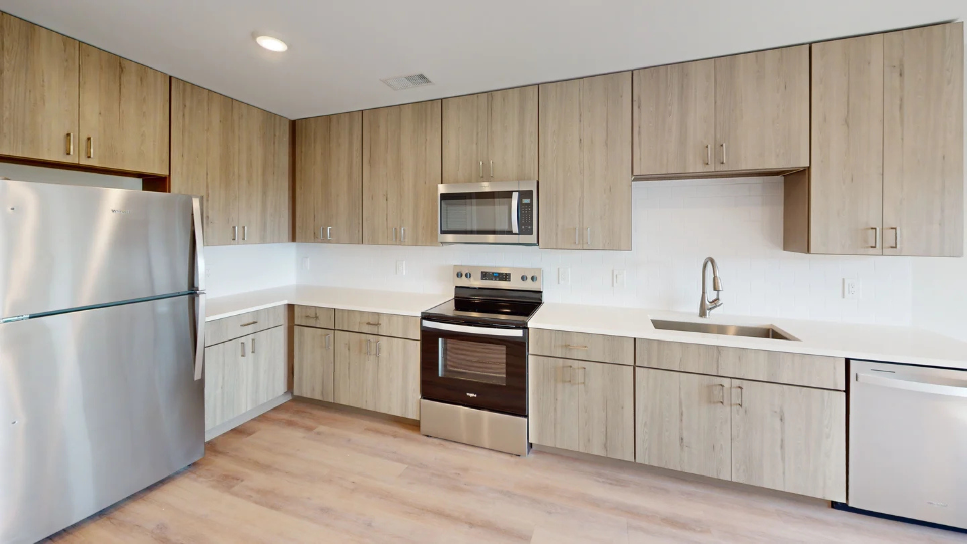 Modern kitchen with stainless steel appliances, light wood cabinets, and white countertops.