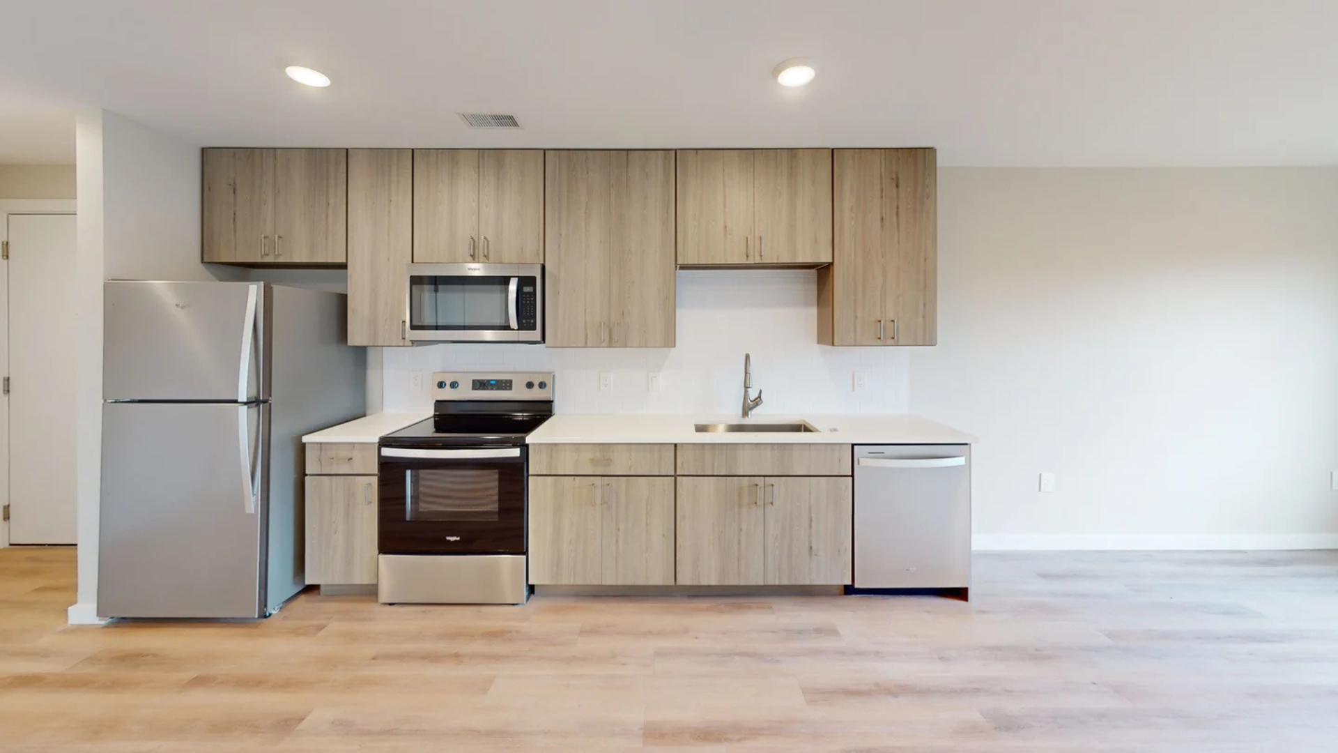 Modern kitchen with stainless steel appliances, light wood cabinets, and light wood flooring.
