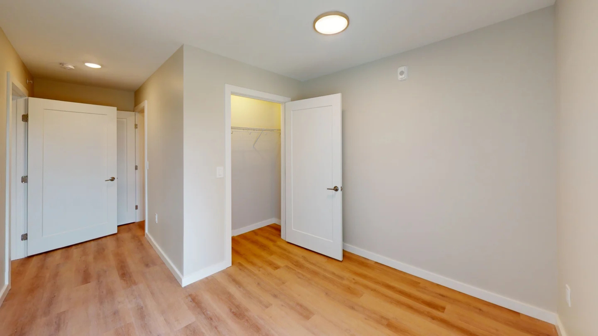 Empty bedroom with light wood flooring, three white doors, and a closet.
