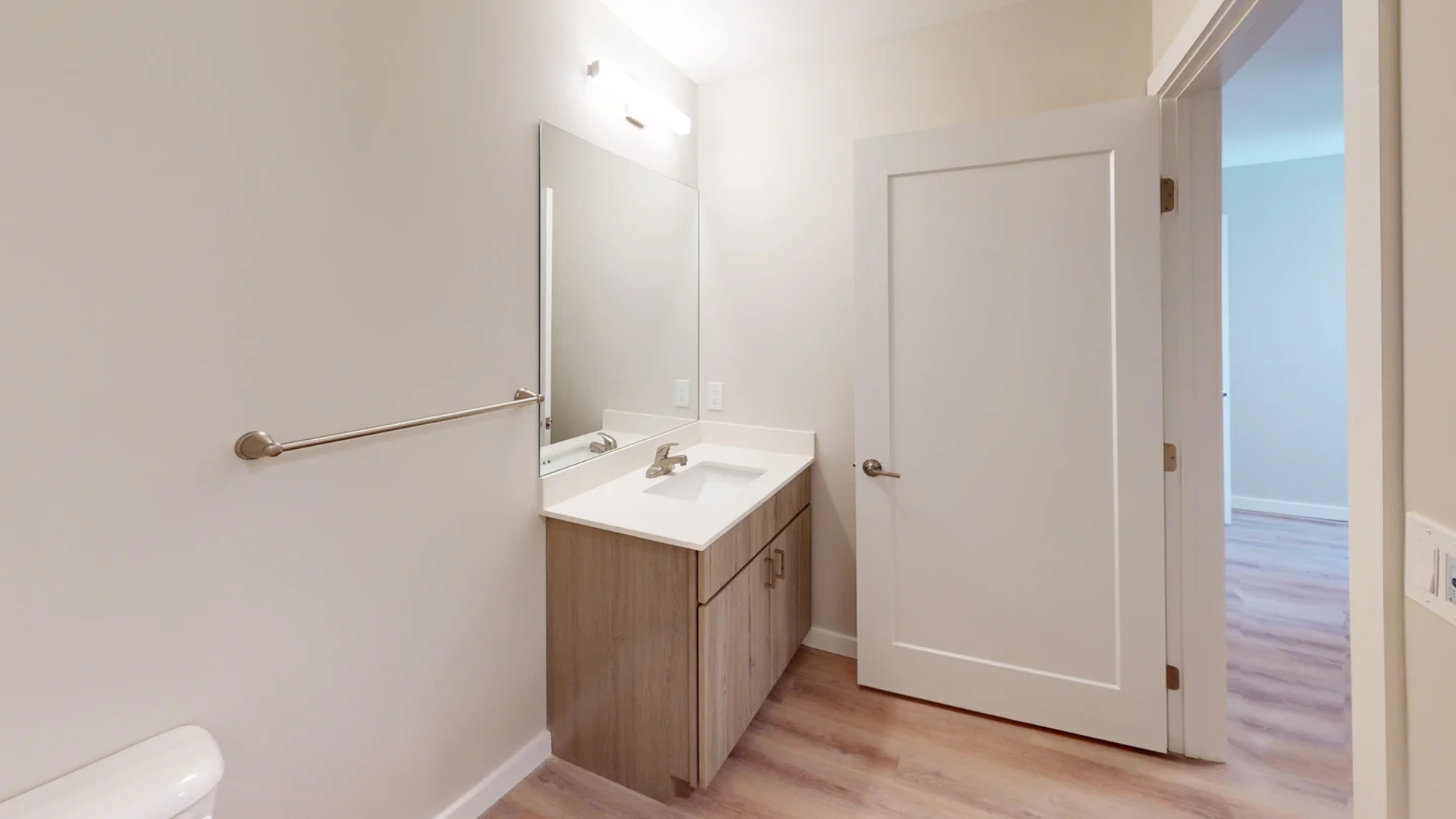 Bathroom with vanity, mirror, and door; light wood cabinet, white countertop, and tan walls.