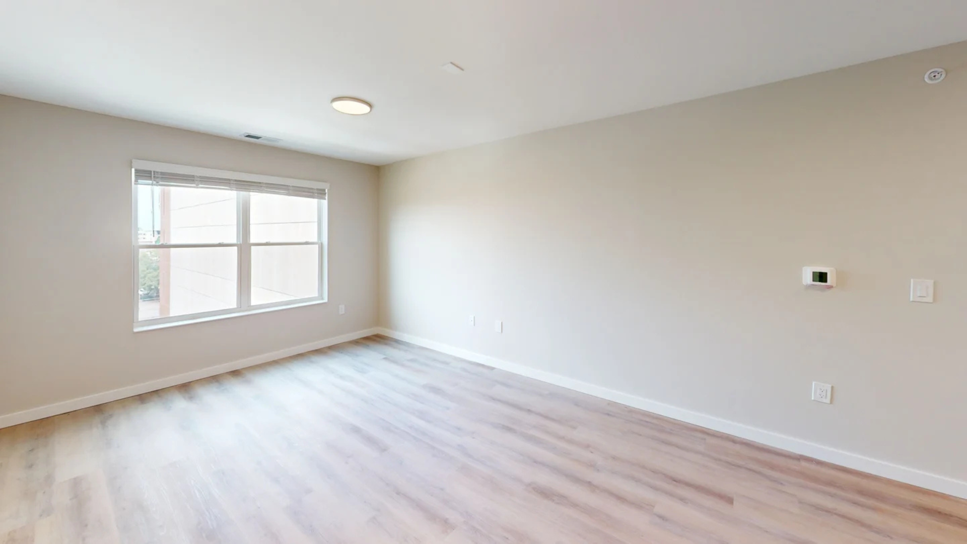 Empty room with wood-look flooring, a window, and beige walls.