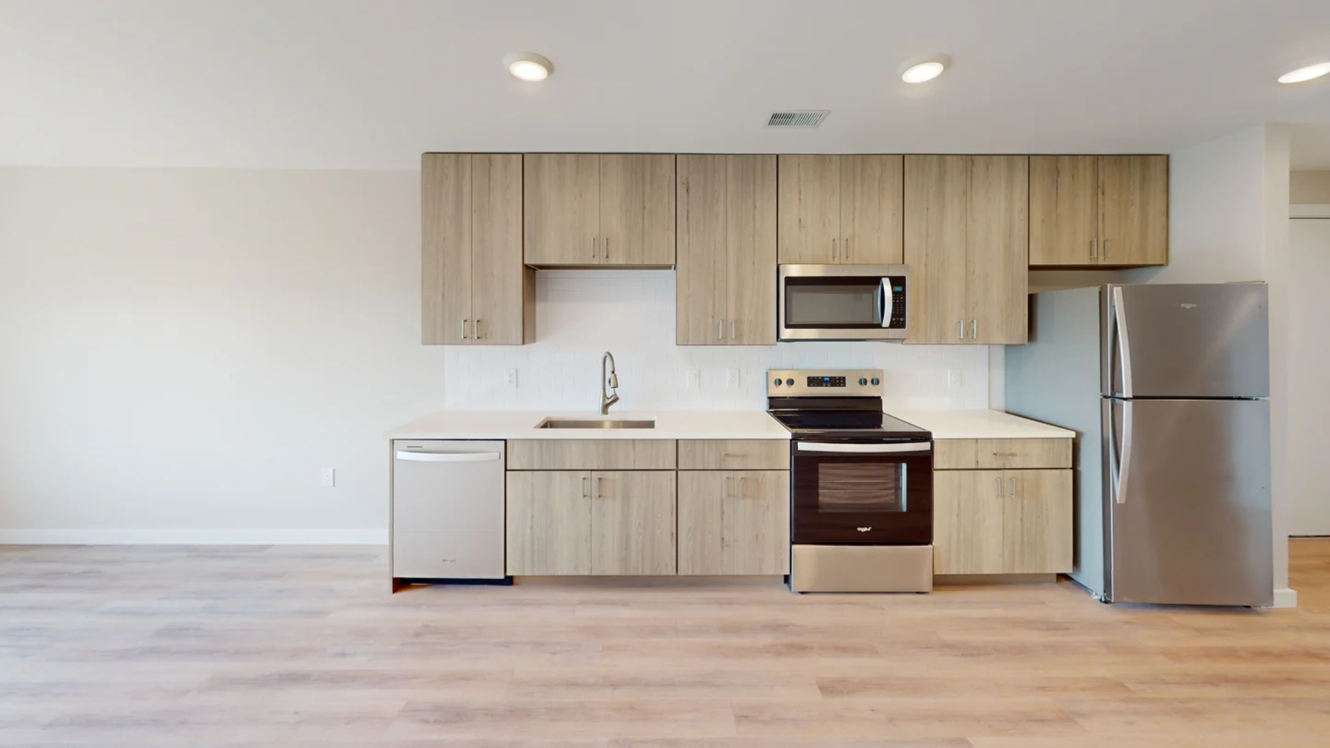 Modern kitchen with light wood cabinets, stainless steel appliances, and white tile backsplash.