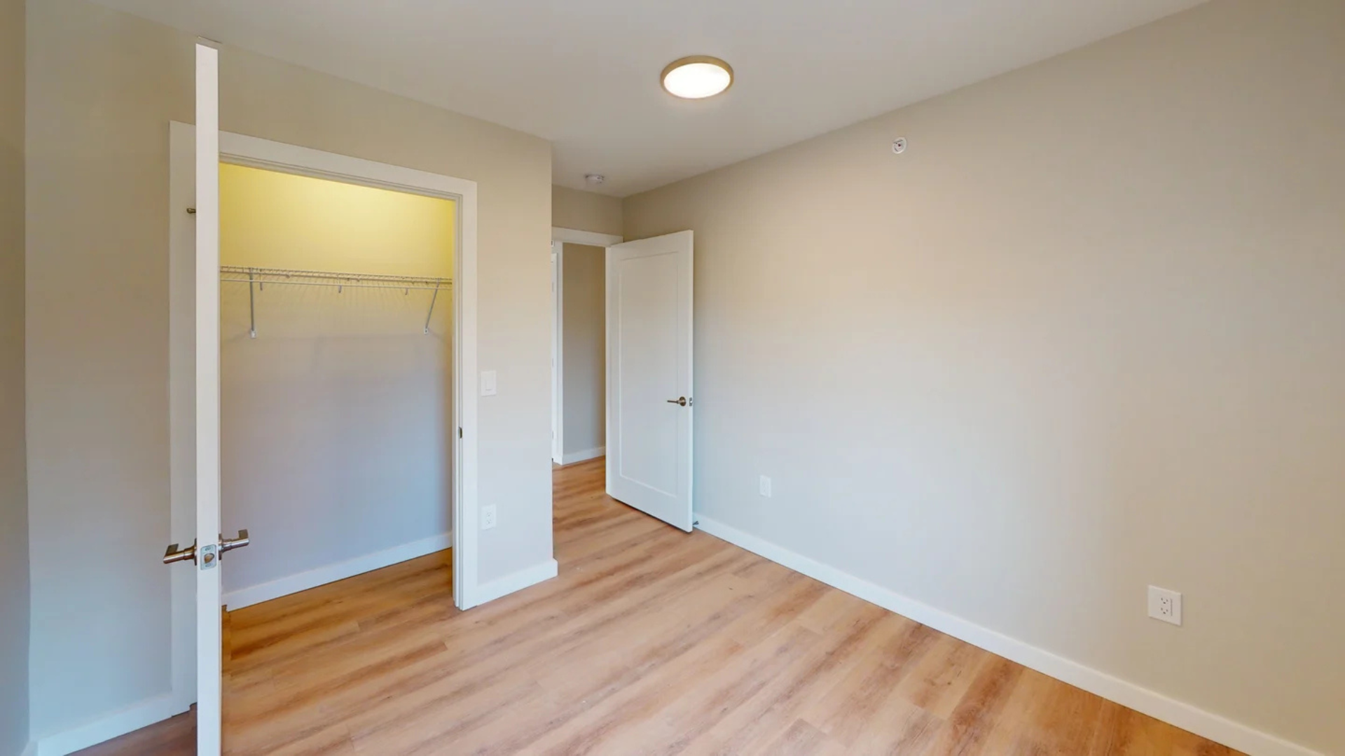 Empty bedroom with light wood floor, closet, and two white doors.