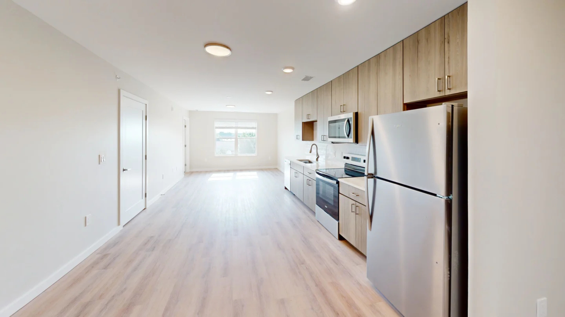 Open-concept kitchen and living area with stainless steel appliances, light wood cabinets, and light wood flooring.