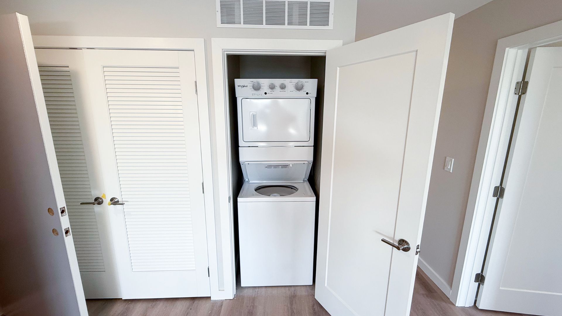 A stacked white washer and dryer in a closet between two white doors.