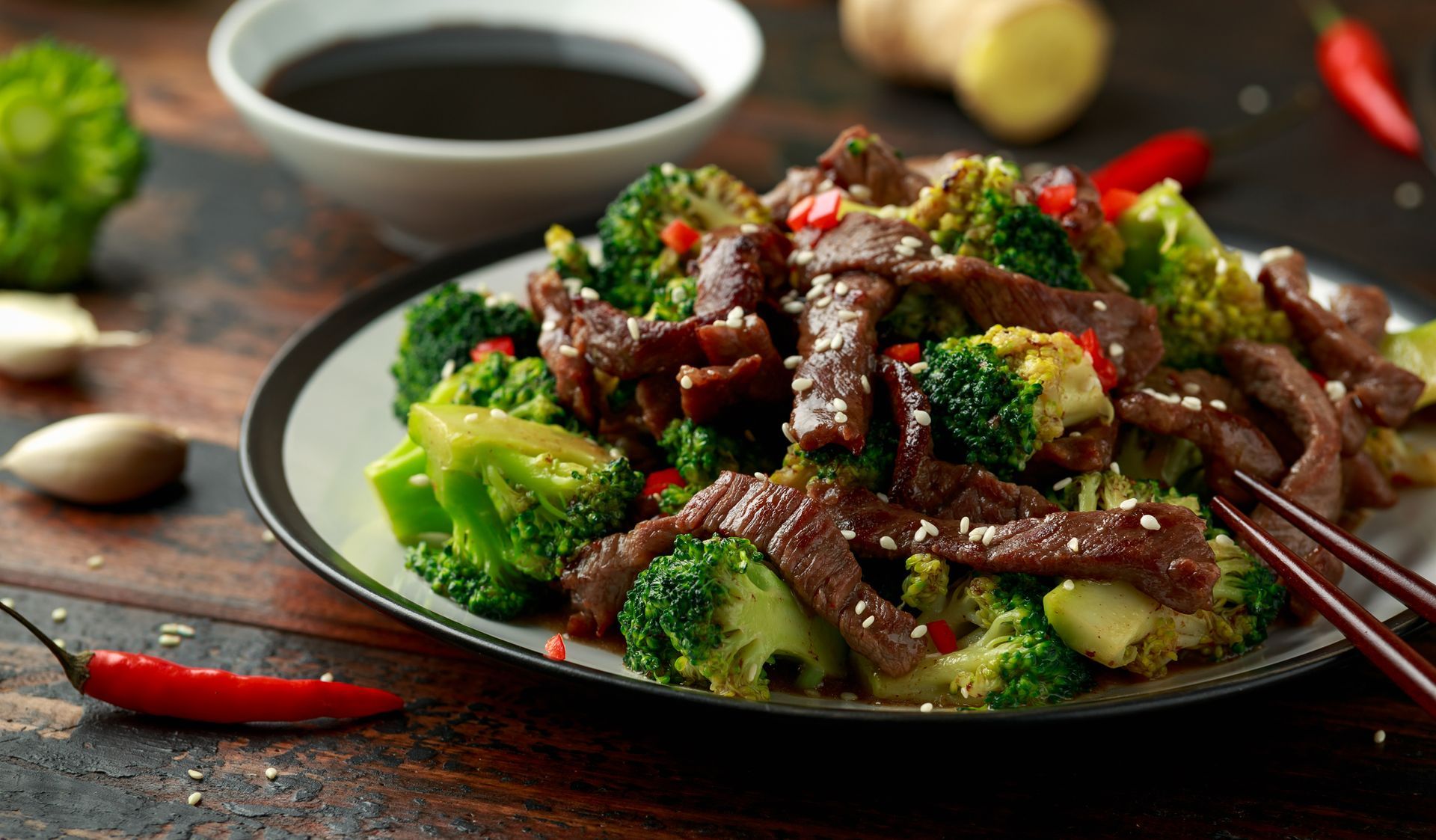 A plate of beef and broccoli with chopsticks on a wooden table.