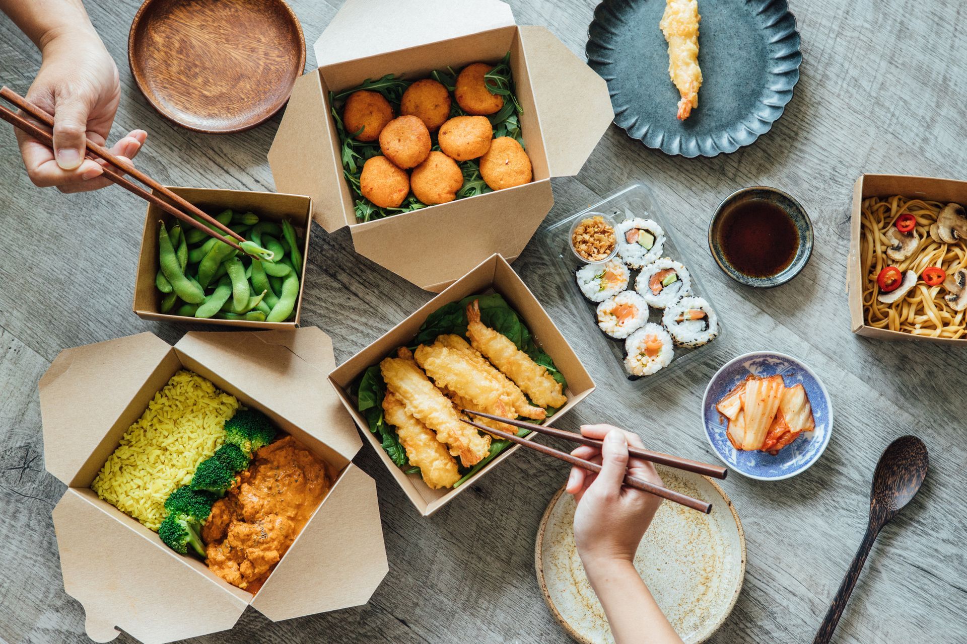 A person is eating food with chopsticks from boxes on a table.