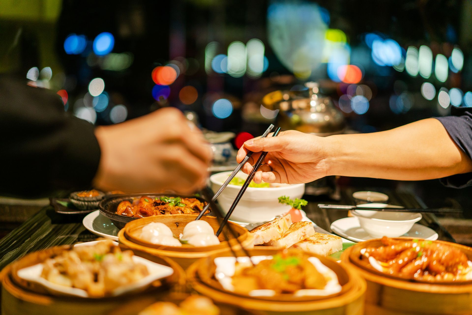 A group of people are sitting at a table eating dim sum with chopsticks.