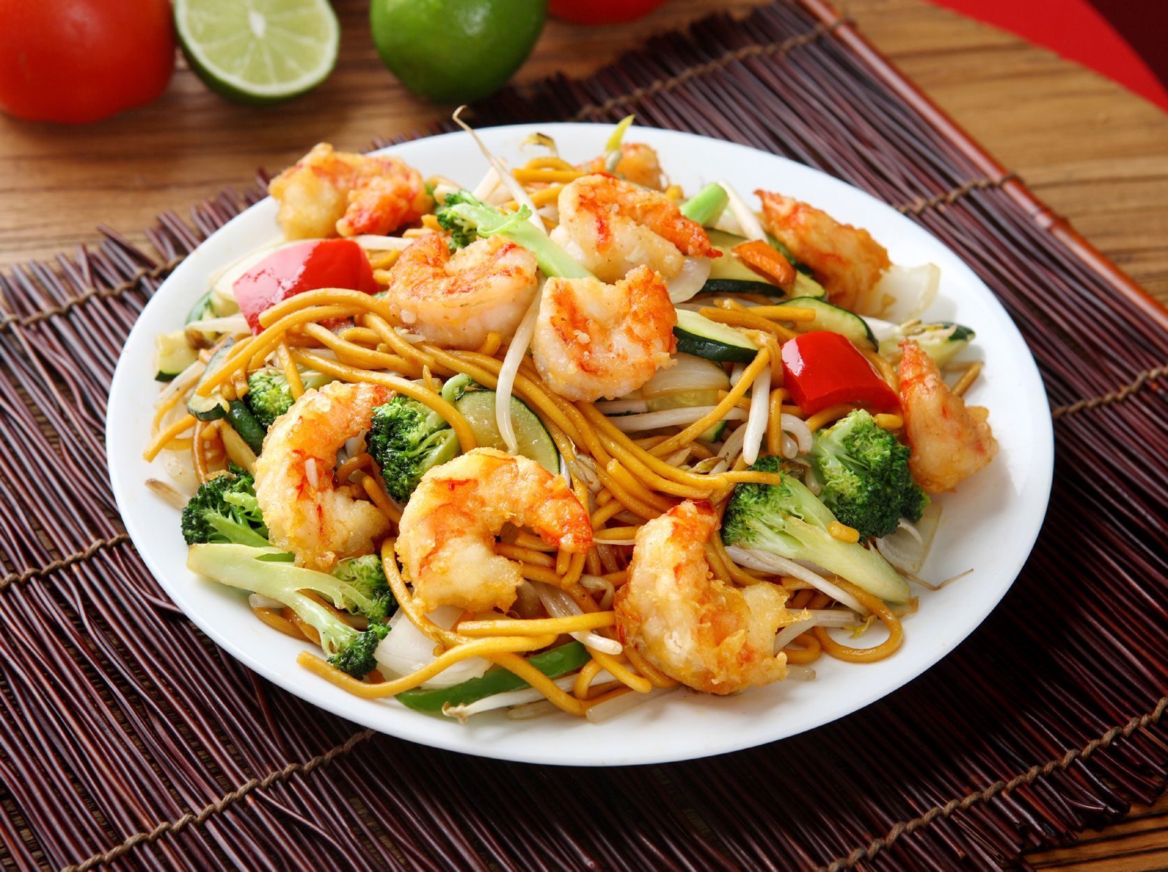 A plate of noodles with shrimp and broccoli on a table.