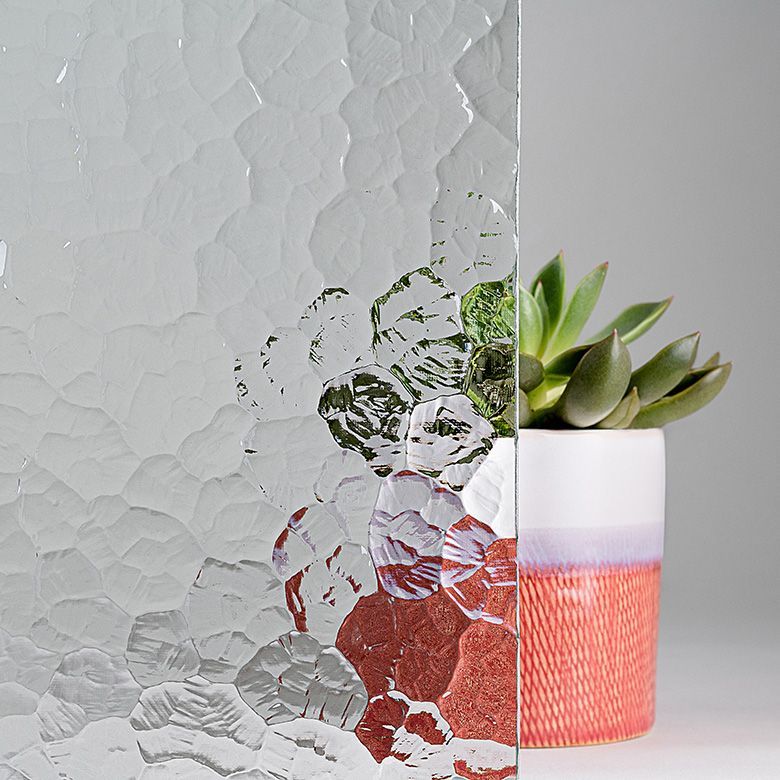 Textured glass sheet partially obscuring a succulent plant in a white and coral pot.