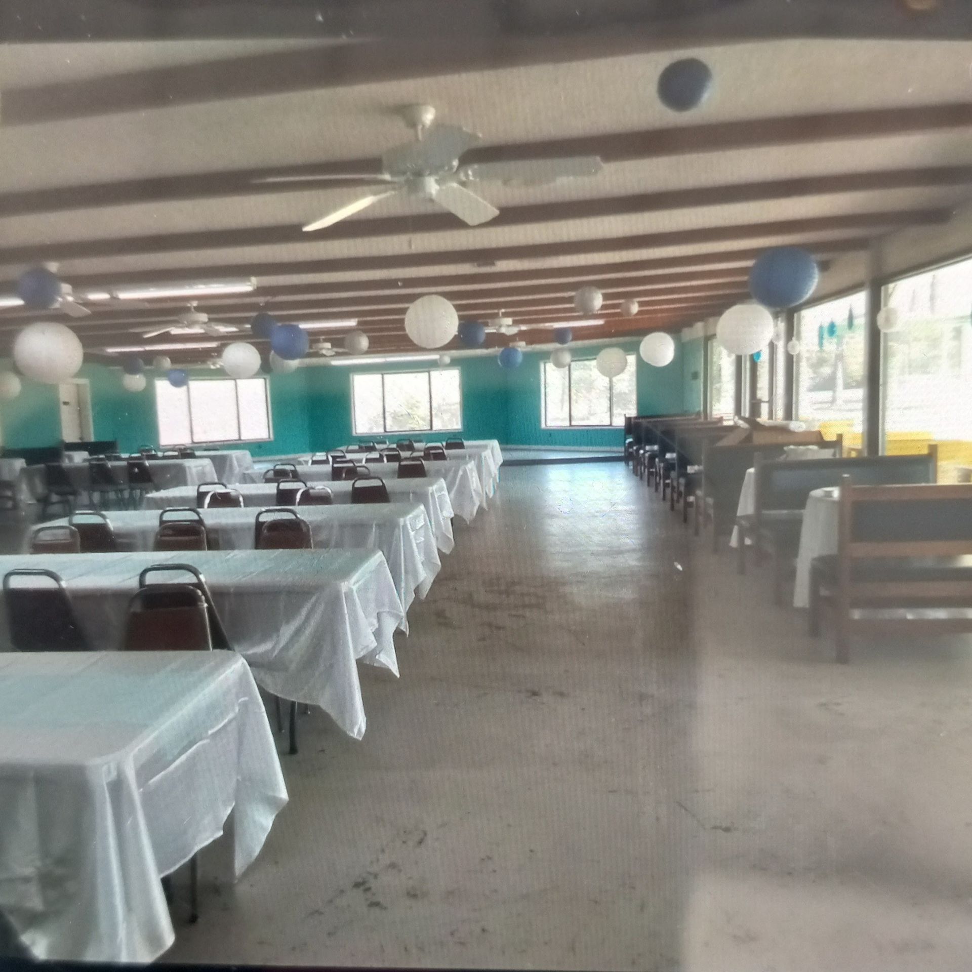 A long room with tables and chairs and balloons hanging from the ceiling