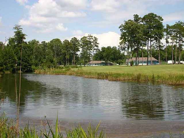 A large body of water surrounded by trees and grass with a house in the background.