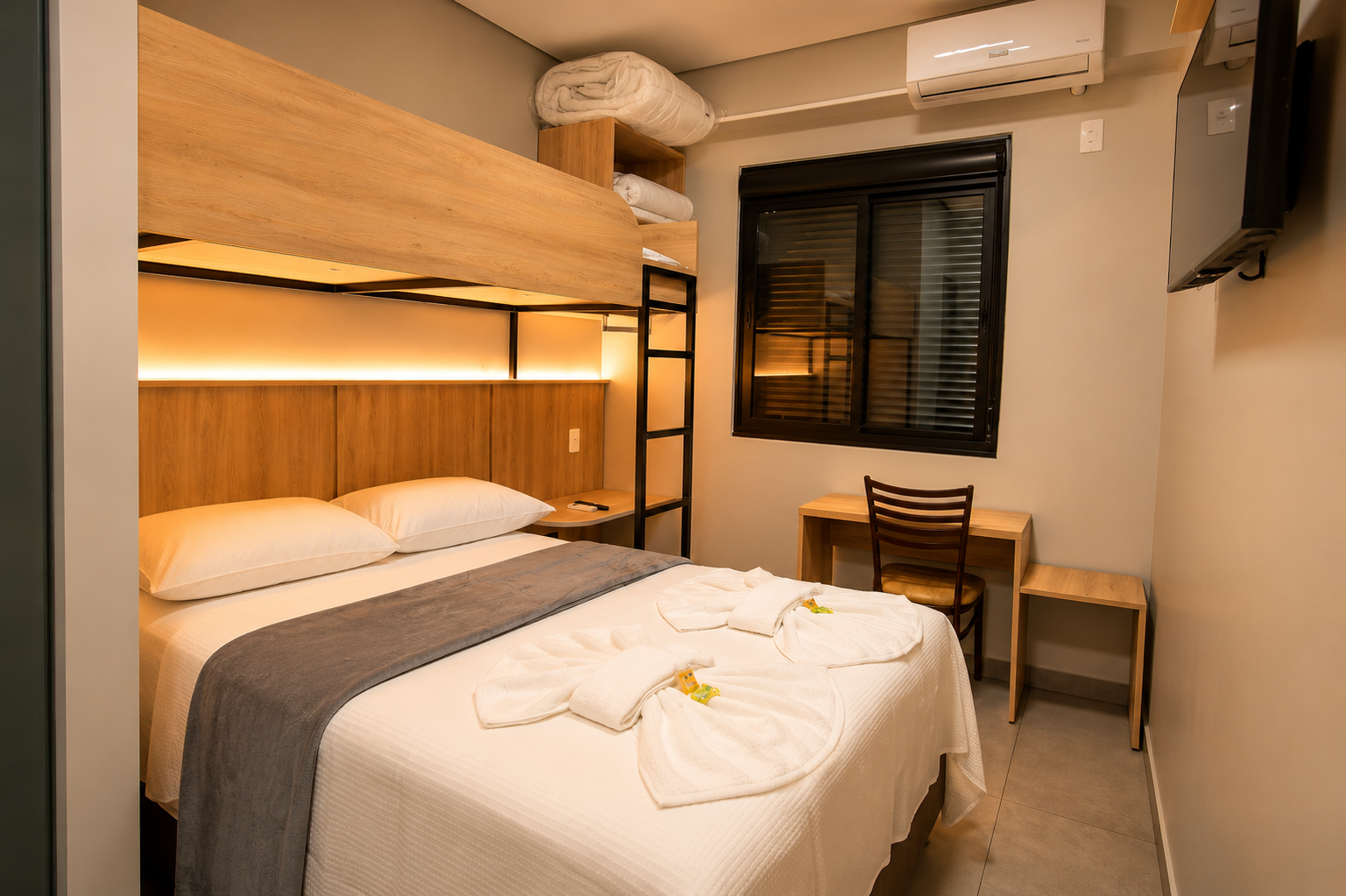 Quarto pequeno com beliche, escrivaninha, persianas e ar-condicionado.