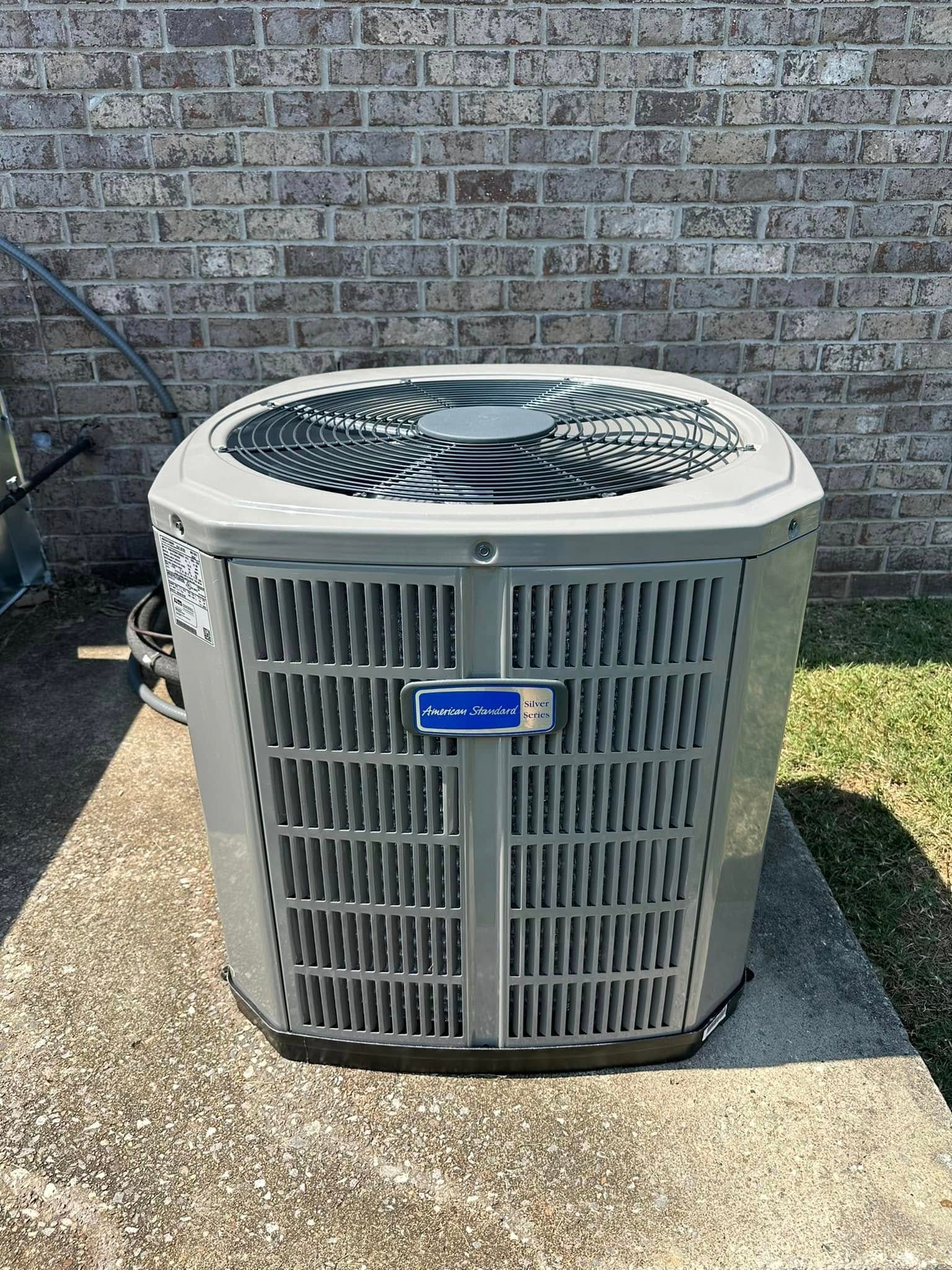 Outdoor central air conditioner unit on a concrete pad against a brick wall.