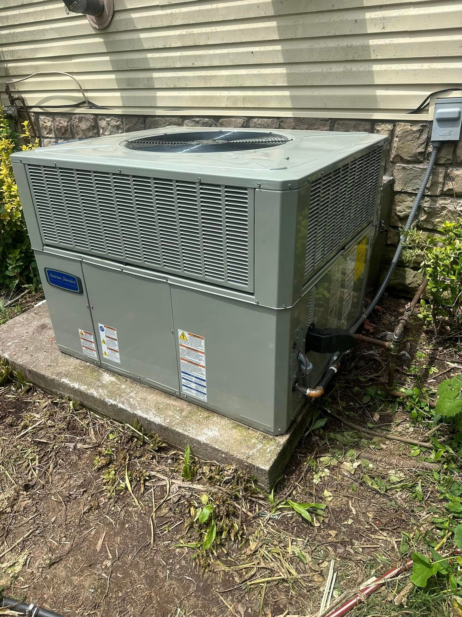 Outdoor gray HVAC unit beside a beige house, surrounded by grass and leaves
