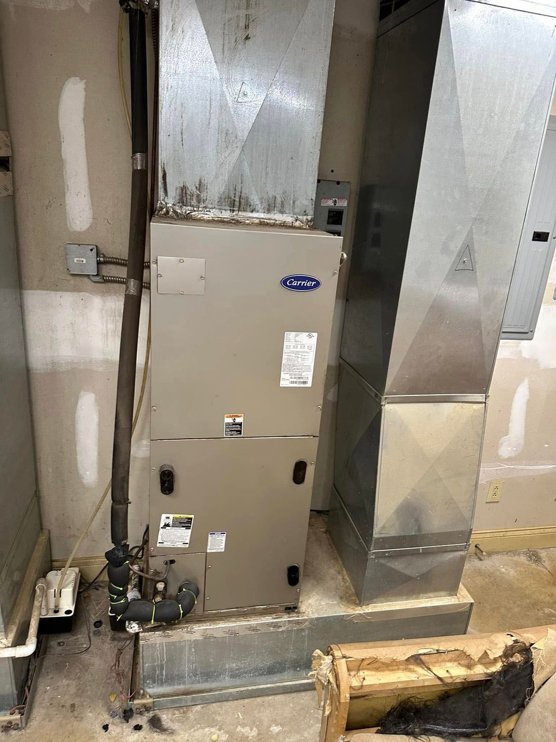 HVAC furnace and metal ductwork in a utility closet with a damaged wooden board on the floor