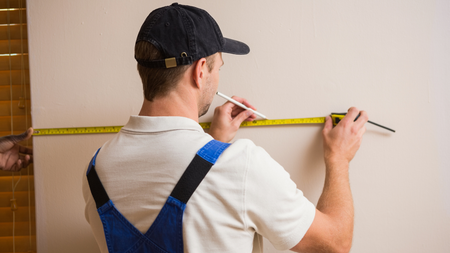 Installer measuring a wall where custom made kitchen cabinets will be mounted.