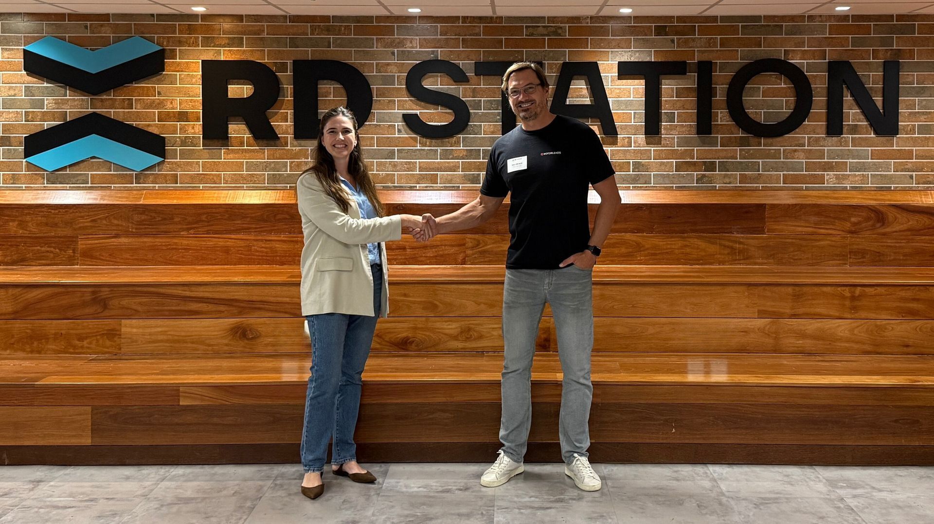 A man and a woman are shaking hands in front of a brick wall.