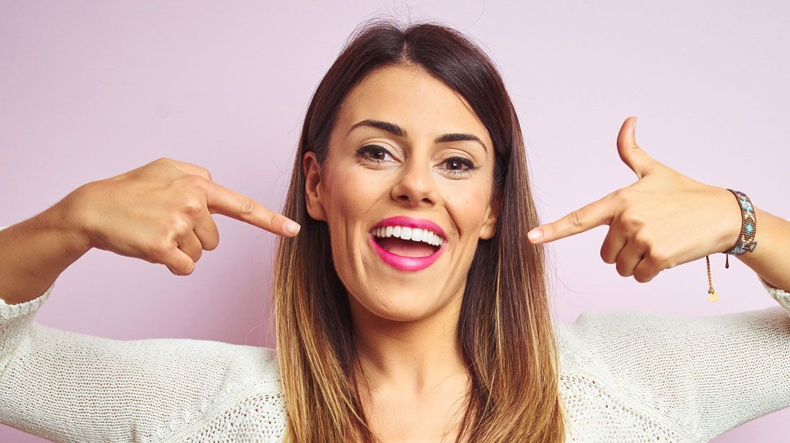 A woman is pointing at her white teeth and smiling.