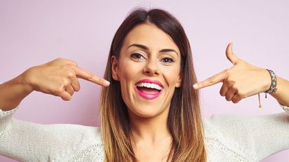 A woman is pointing at her white teeth and smiling.