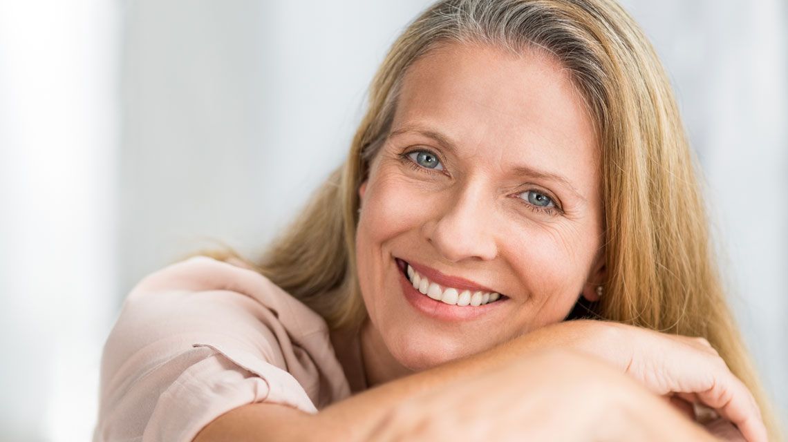 A close up of a woman smiling with her hands on her shoulder.