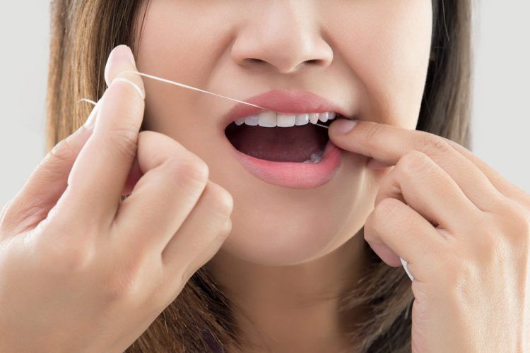 A woman is flossing her teeth with a dental floss.