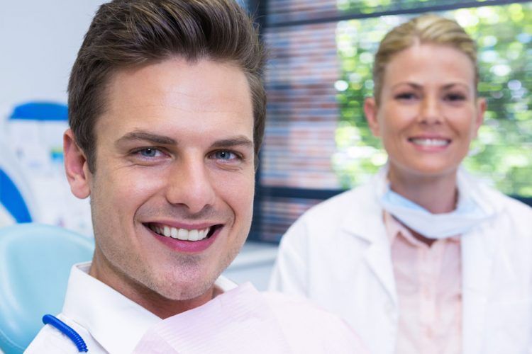 A man is smiling while sitting in a dental chair next to a female dentist.