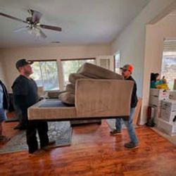 A man is carrying a couch in a living room.