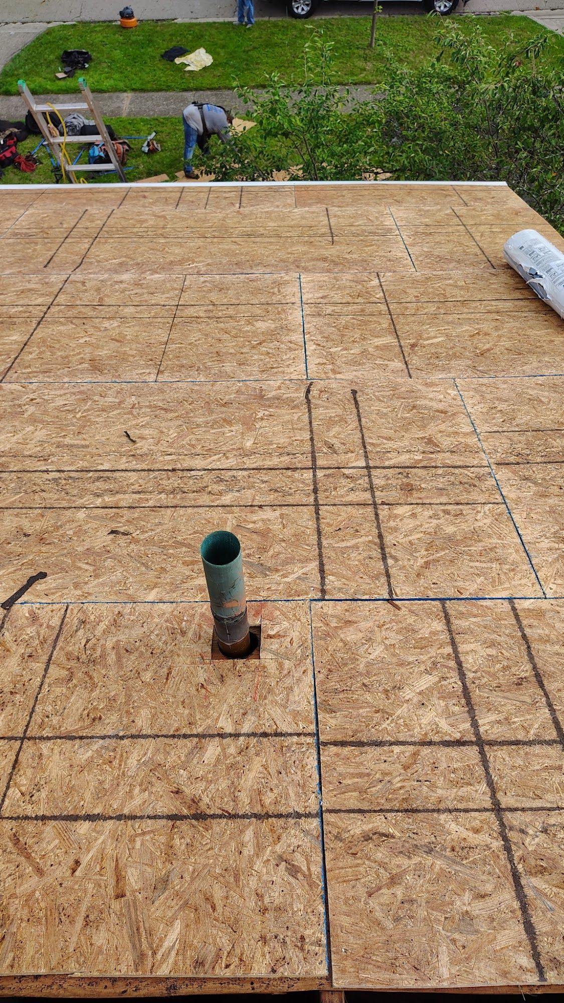 OSB roof with plumbing vent, workers in background.