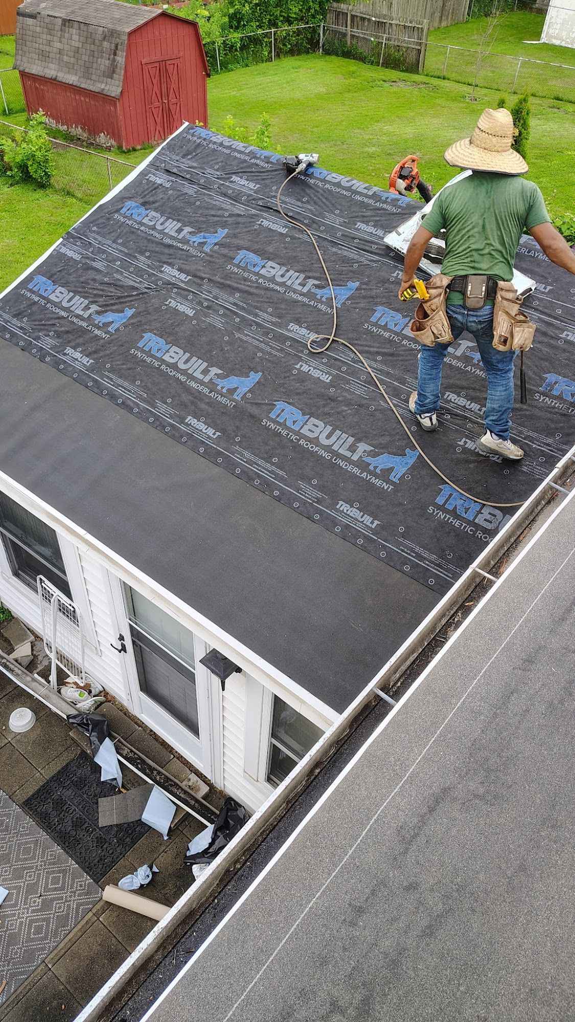 A roofer in a straw hat works on a roof covered with black roofing underlayment.