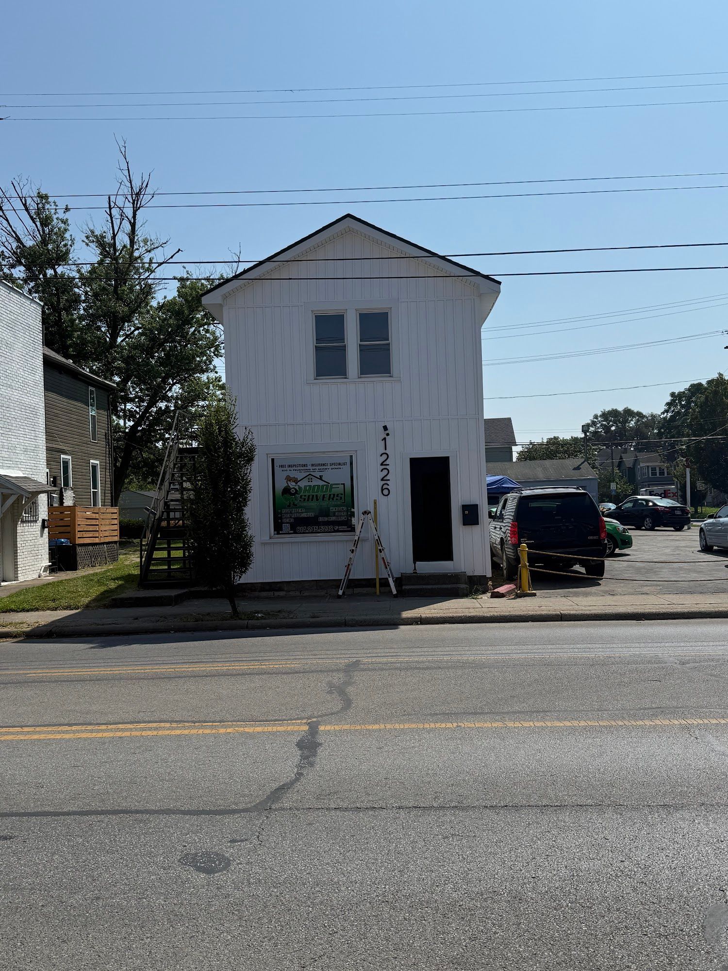 White two-story building with black door, window, and business sign at the front. Cars are parked nearby.