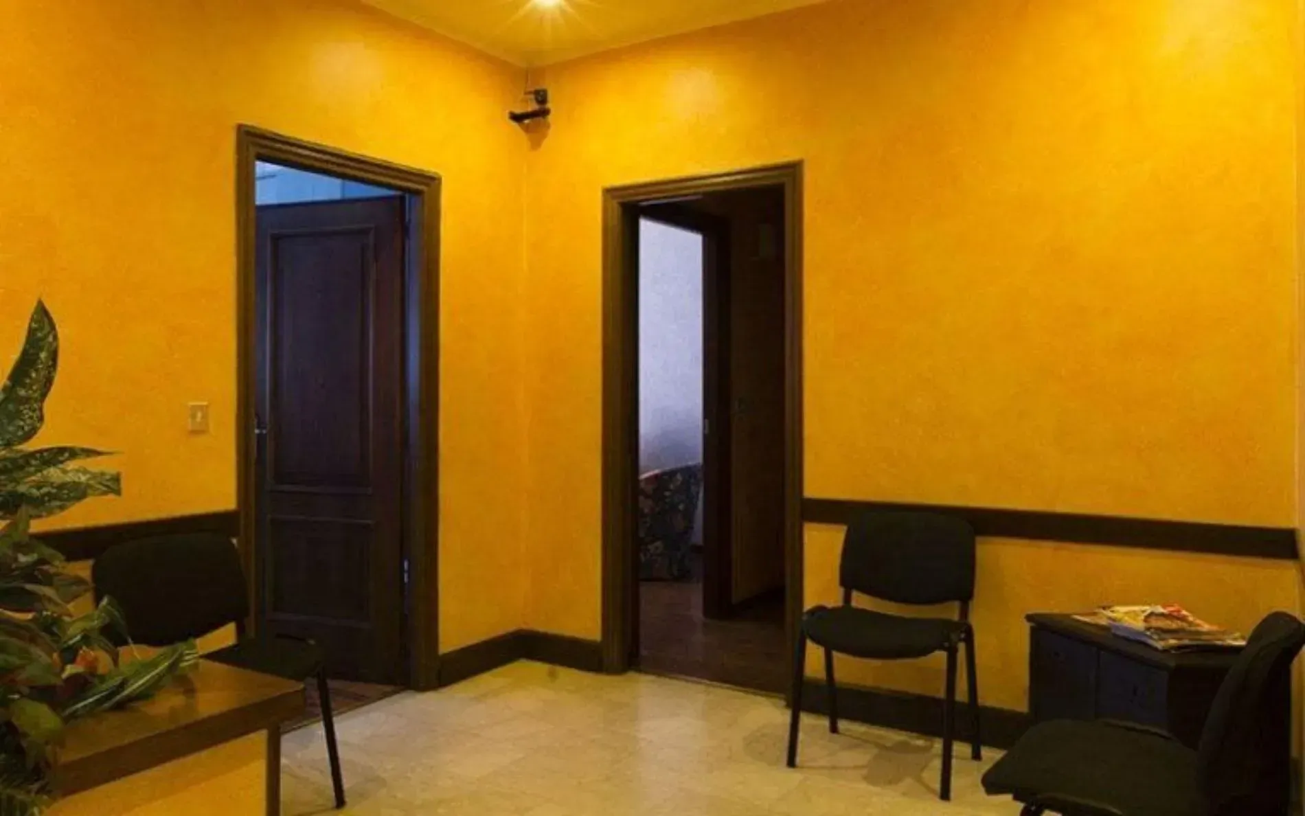 Stanza con pareti gialle, due porte aperte, sedie scure e un tavolino.