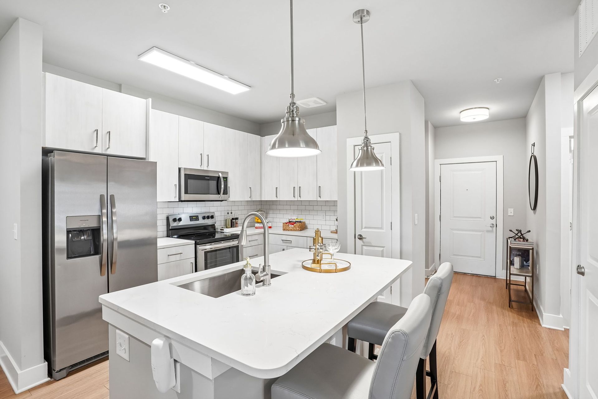 Bright modern kitchen with white island, stainless appliances, and gray chairs