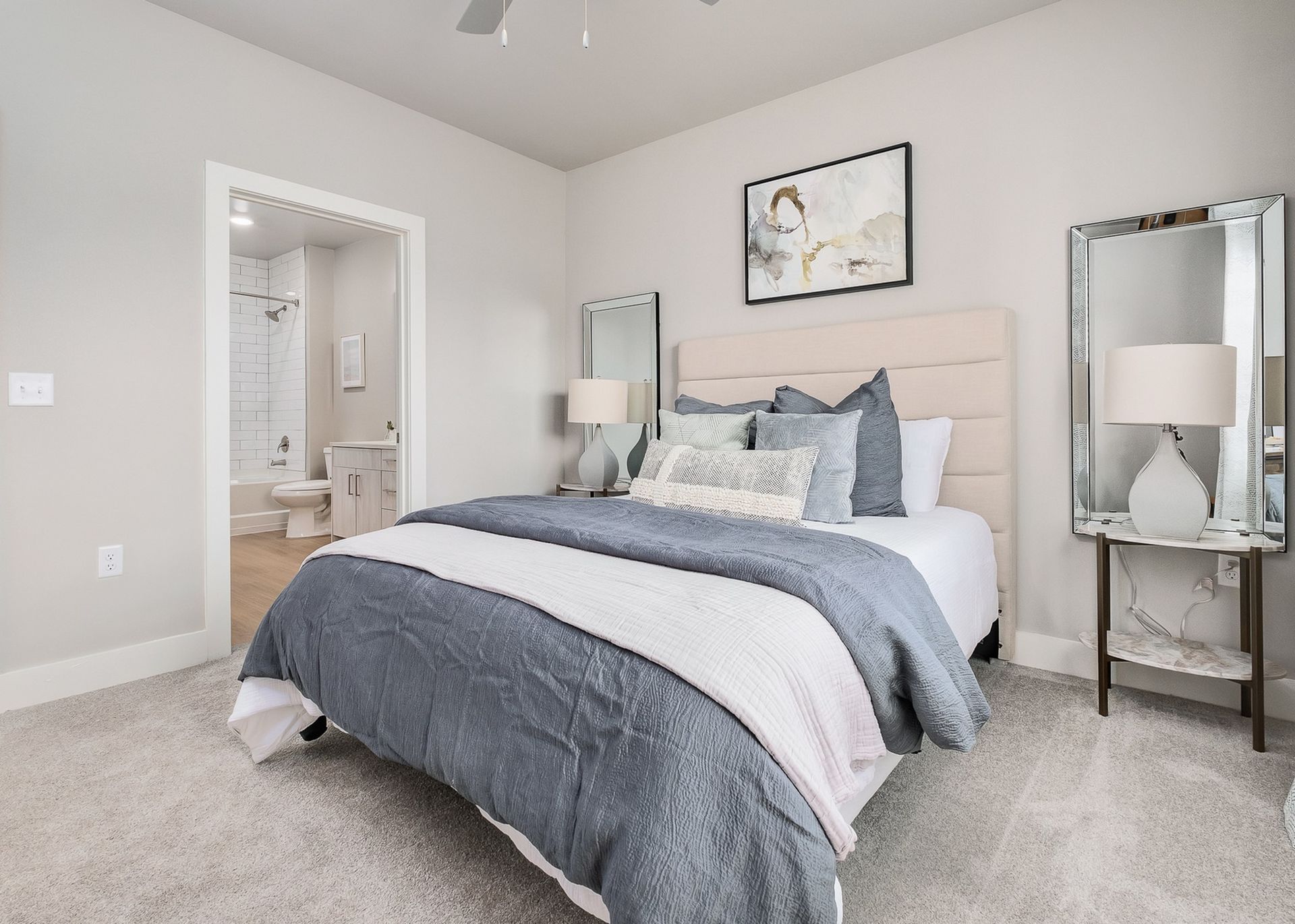 A bedroom with a large bed , two lamps , a mirror and a ceiling fan.