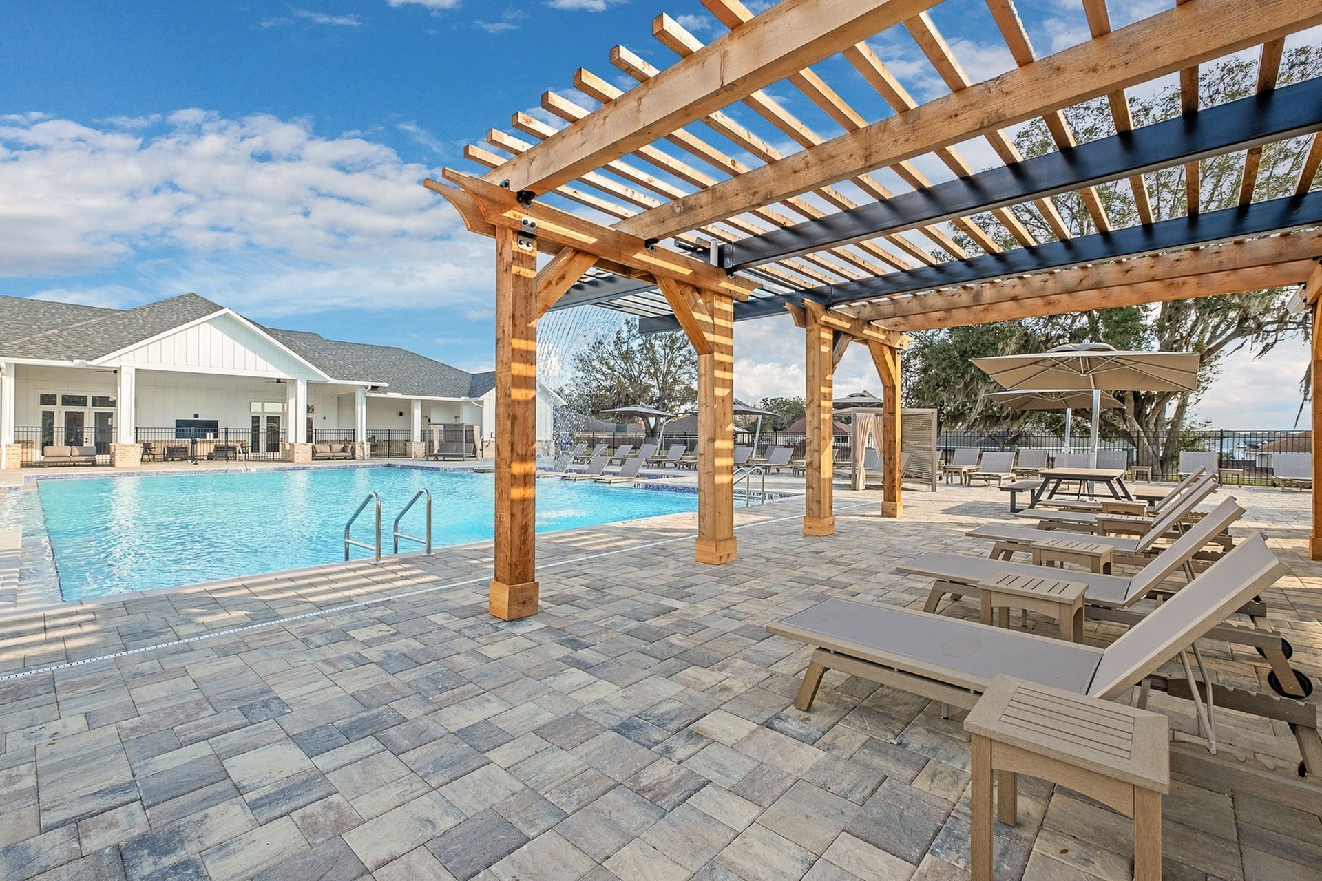 A swimming pool with a pergola and lounge chairs in front of it.
