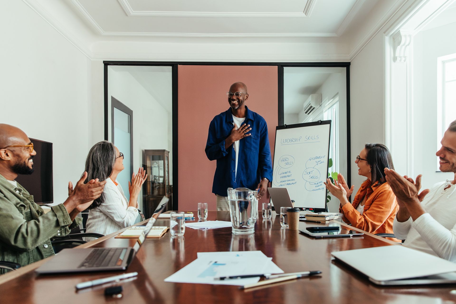 Team meeting in a conference room, with a presenter at a whiteboard and colleagues applauding.