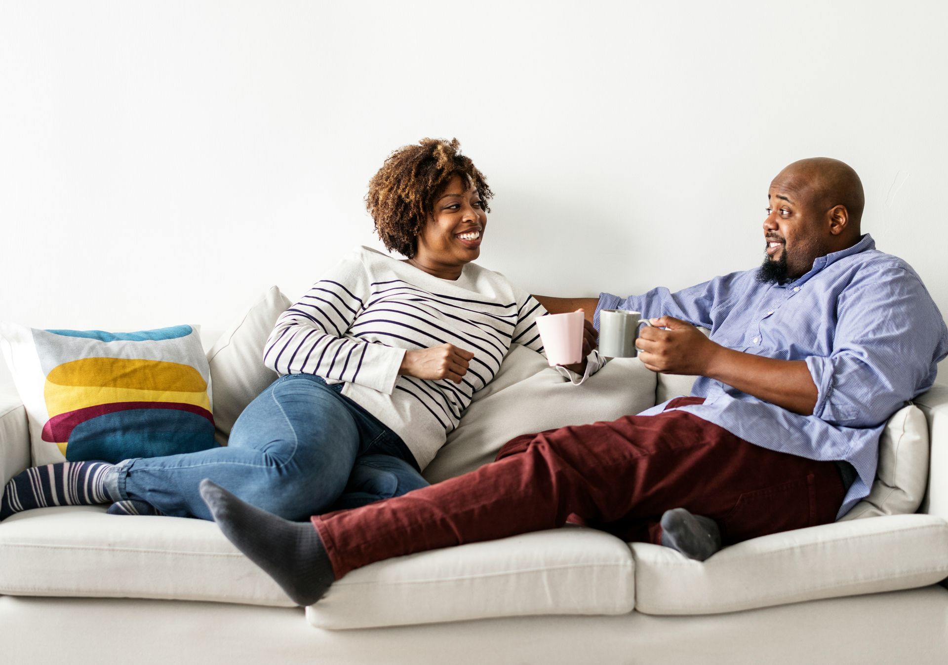A man and a woman are sitting on a couch drinking coffee.