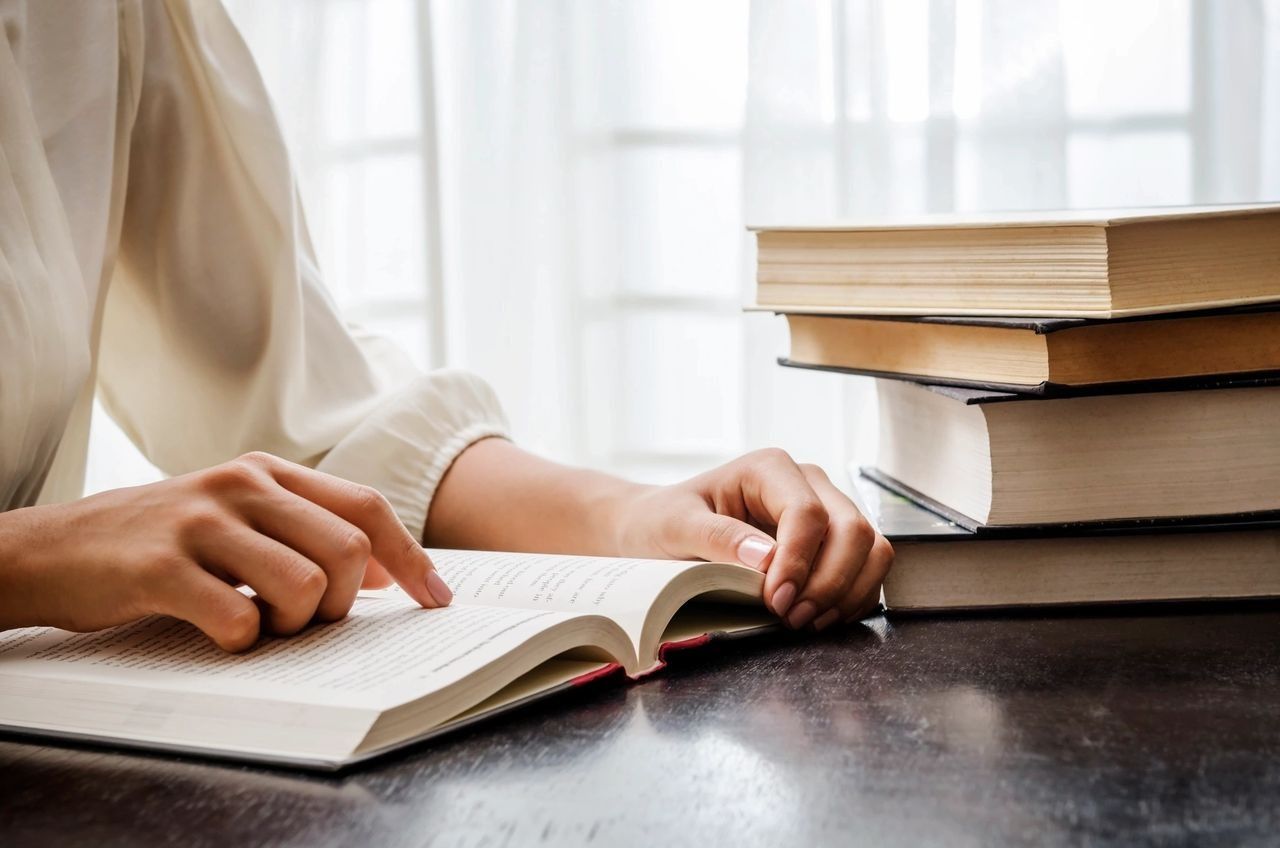 A Woman Is Reading A Book On A Table Next To A Stack Of Books — Phoenix Mandorla In Rockhampton City, QLD