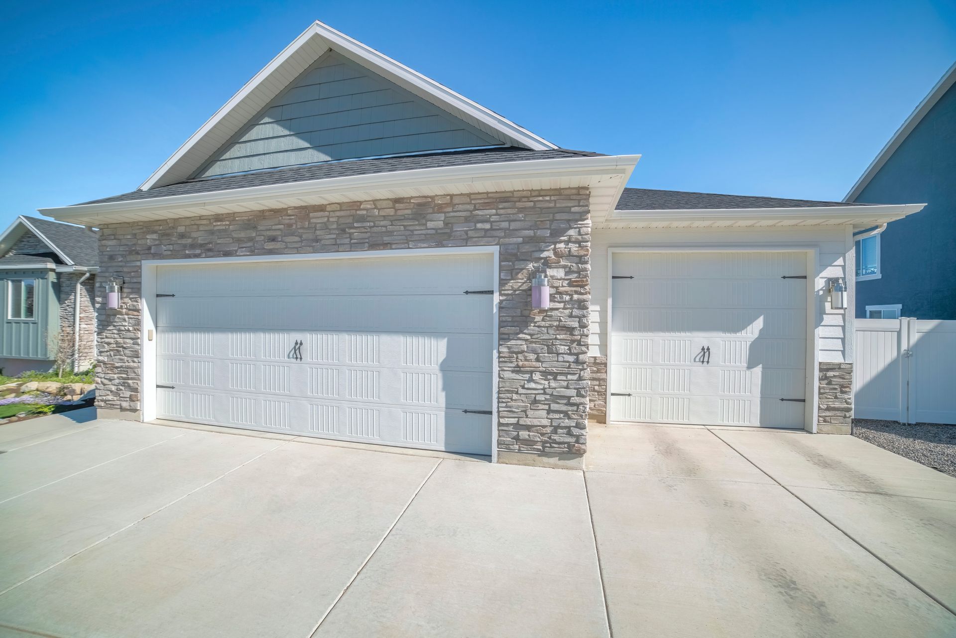 Two-car garage with white doors, stone accents, and a concrete driveway under a blue sky.
