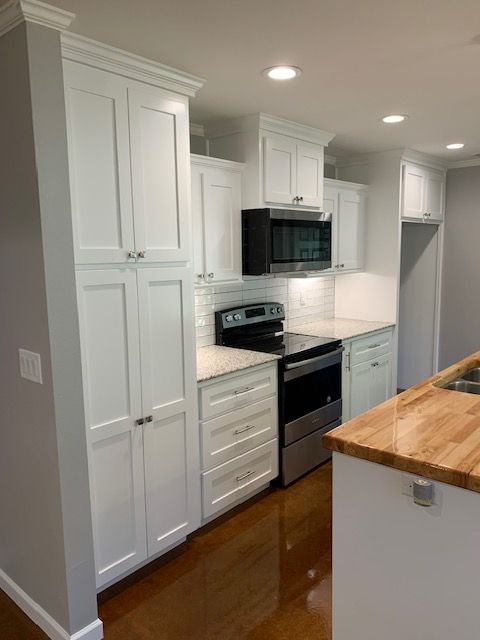 A kitchen with white cabinets , stainless steel appliances , and a wooden counter top.