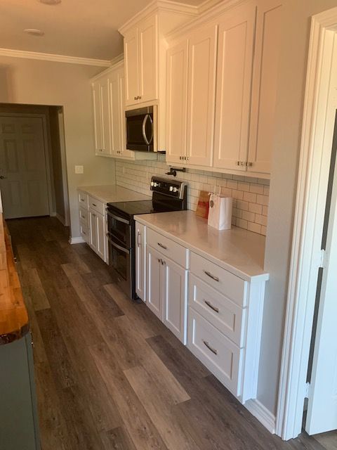 A kitchen with white cabinets , a stove , and a microwave.