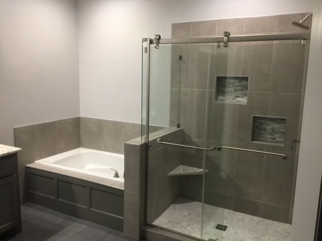 A bathroom with a tub and a shower with sliding glass doors.