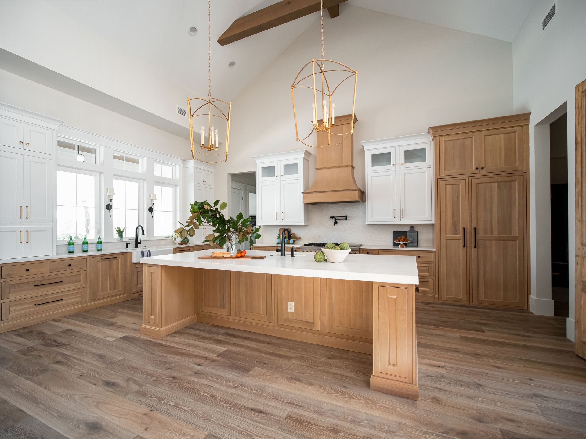 A modern, high-ceilinged kitchen featuring a large wooden island, white upper cabinets, and warm wood flooring.
