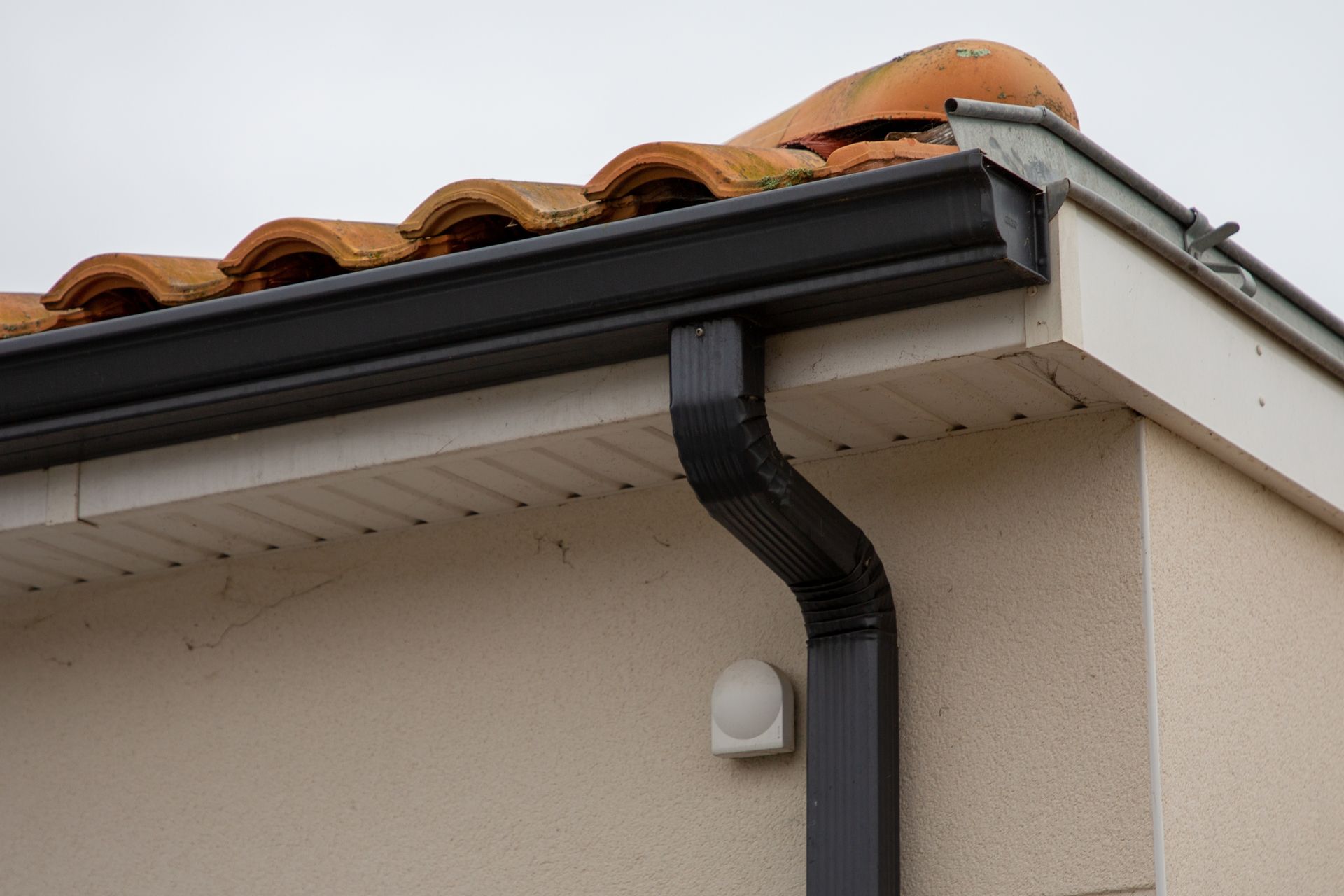 Black guttering on a roof, with terracotta tiles, against a cream-colored wall.